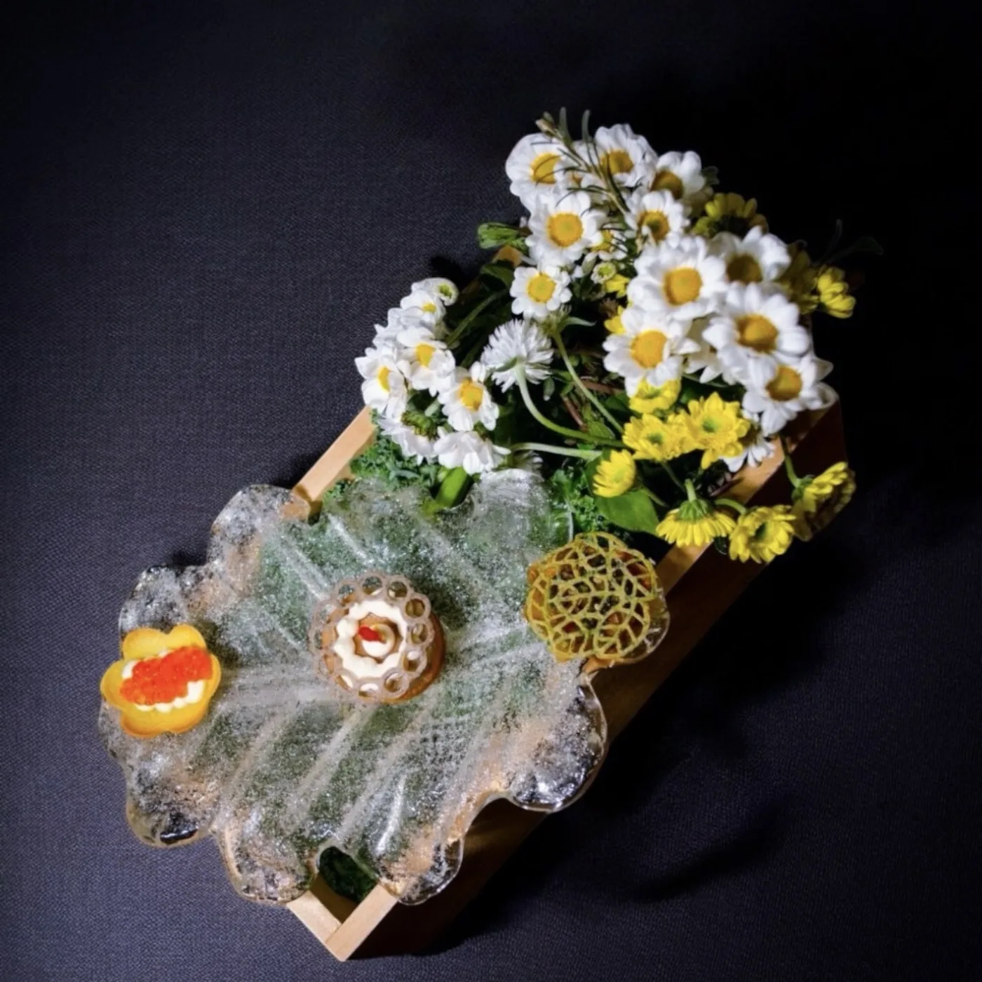 Bocado de autor con flores de estación sobre soporte de hielo en A Fuego Fuerte