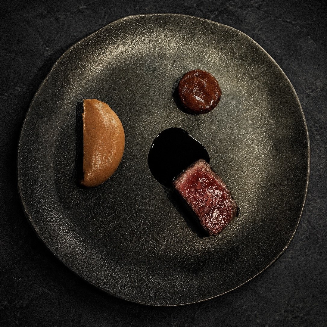 Plato de autor: corte de carne con reducción y puré sobre vajilla oscura en A Fuego Fuerte